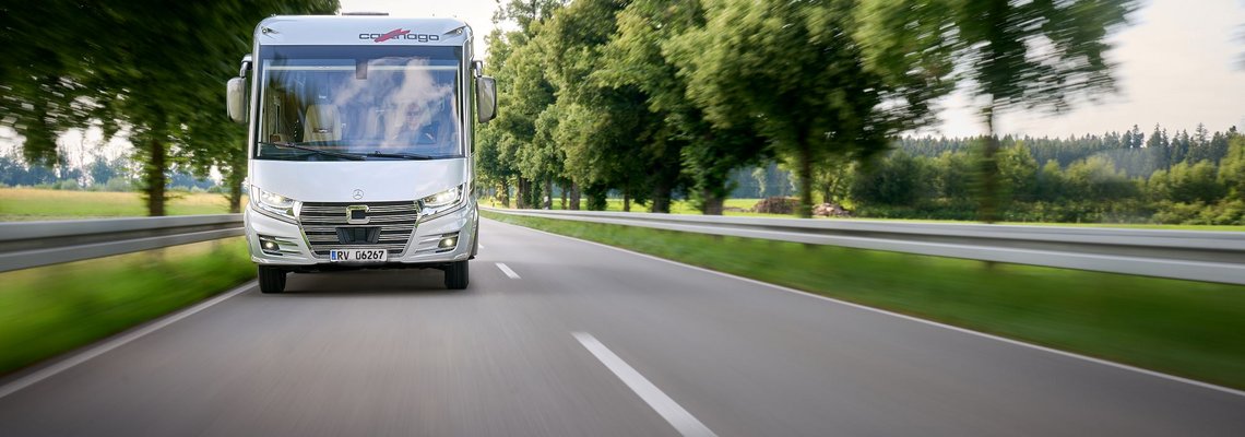 Ansicht eines Carthago Wohnmobils auf einer Landstraße zwischen Bäumen und Wiesen.